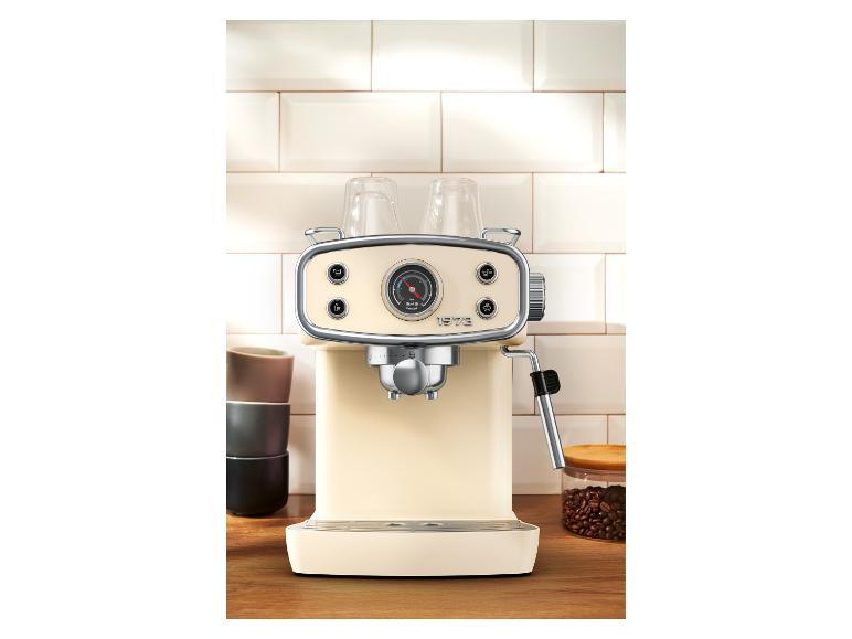 Cremefarbene Retro-Kaffeemaschine mit Manometer, auf einer Holzarbeitsplatte mit Tassen und Kaffeebohnen.