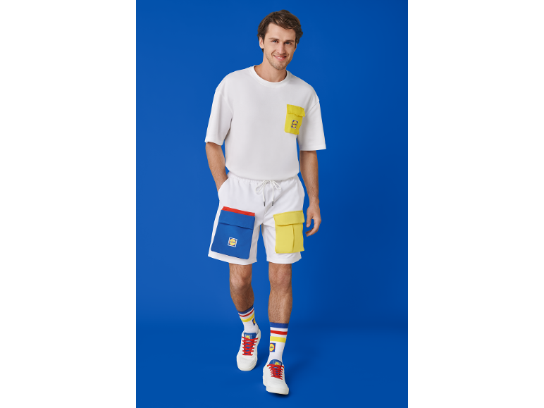 Mann in weißem T-Shirt, weißen Shorts mit farbigen Taschen und Turnschuhen.