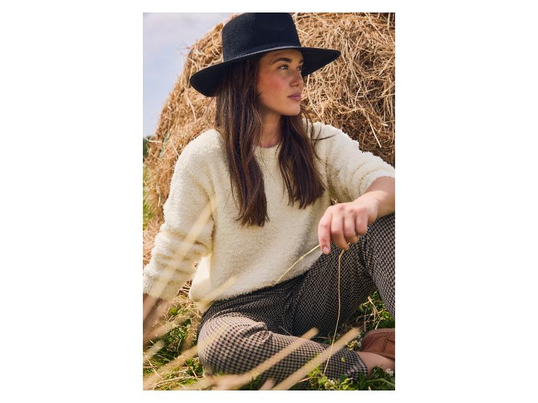 Frau in cremefarbenem Pullover und Hahnentritt-Hose sitzt an Heuballen.