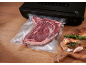 Vakuumverpacktes Steak mit Vakuumiergerät und Gewürzen auf Holzbrett.