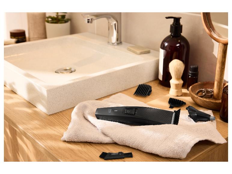 Haarschneider und Zubehör auf einem Handtuch in einem Badezimmer mit Waschbecken.