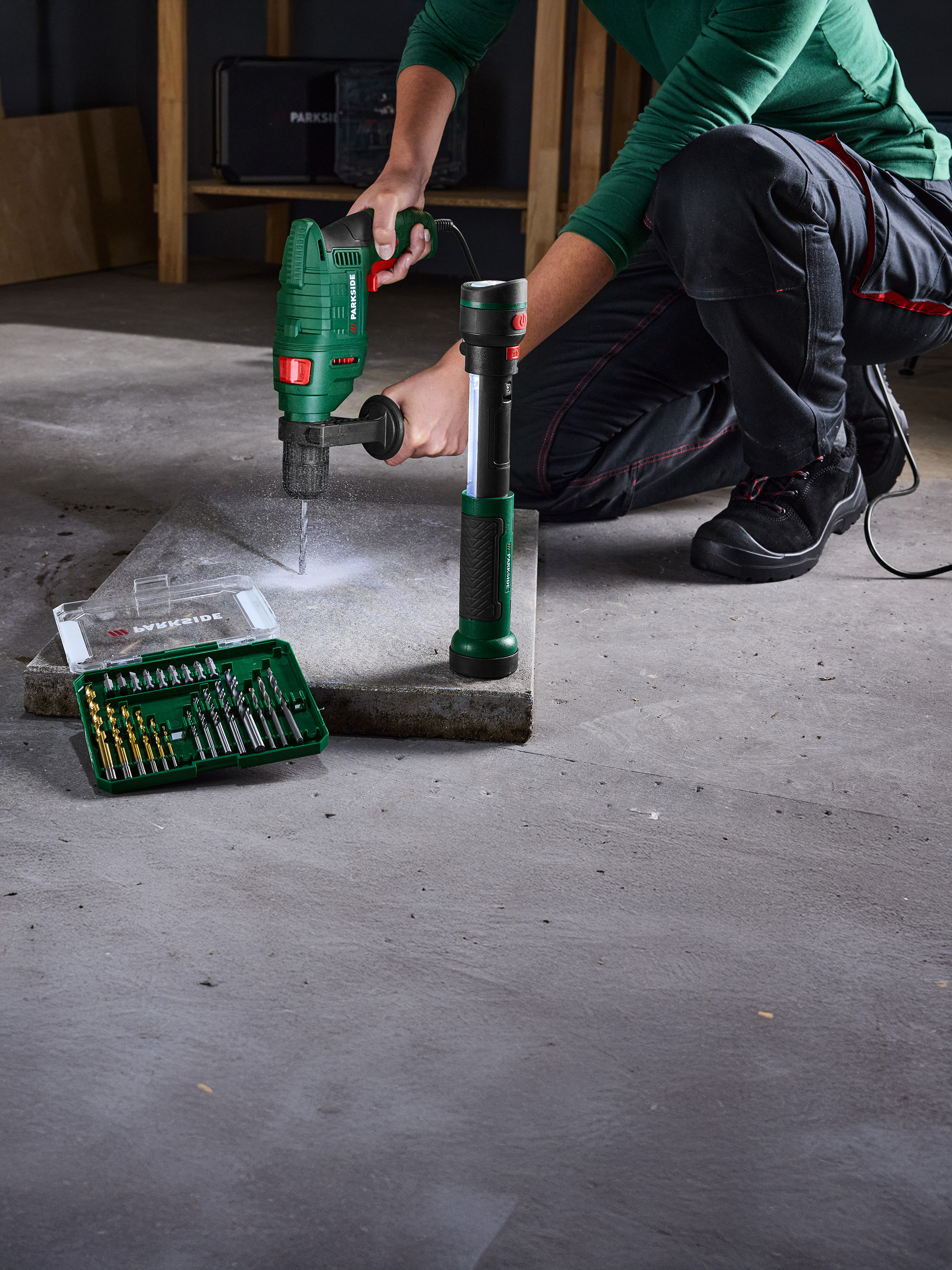 Eine Person benutzt eine Parkside Bohrmaschine, um in eine Betonplatte zu bohren, mit einem Bohrersatz daneben.
