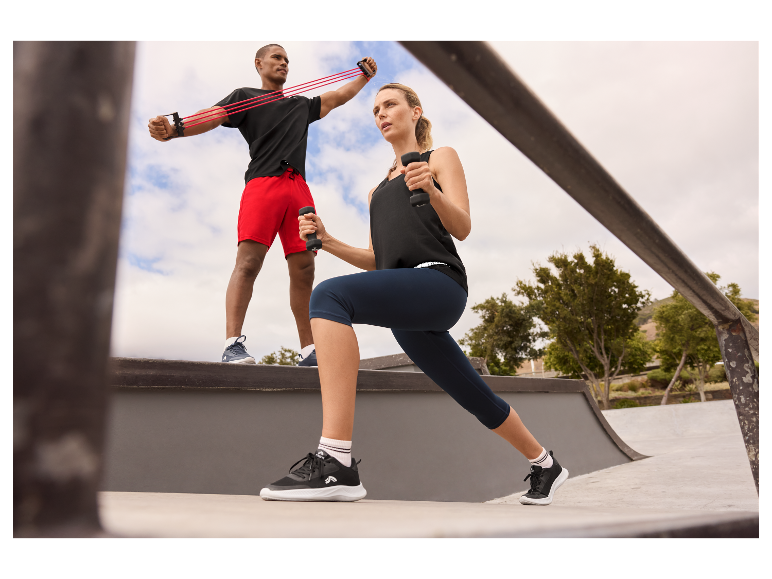 Mann und Frau trainieren mit Gummibändern und Hanteln im Freien.