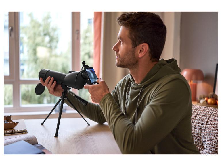 Ein Mann benutzt ein schwarzes Teleskop mit einem Smartphone auf einem Stativ.