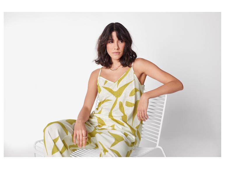 Frau sitzt auf einem weißen Stuhl in einem grün-weißen Leinen-Ensemble.