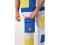 Detail eines Mannes in weißer Weste und Hose mit blauen und gelben Taschen, der eine Tasche mit rotem Reißverschluss öffnet.
