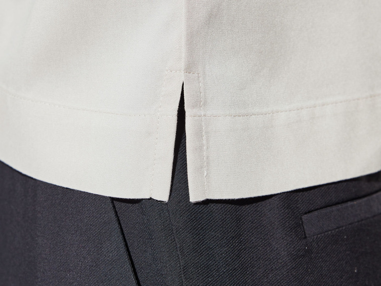 Nahaufnahme eines beigen Hemdes mit Schlitzen, getragen zu einer schwarzen Hose.