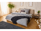 Schlafzimmer mit beigem Bett, grauer Bettwäsche mit Bäumen, dunkelgrauer Decke und Teppich.