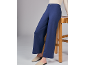 Frau in blauer, weit geschnittener Hose, die an einem Holzhocker lehnt.