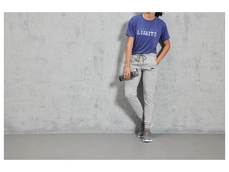 Model mit blauem T-Shirt und grauen Jogginghosen hält eine Wasserflasche.