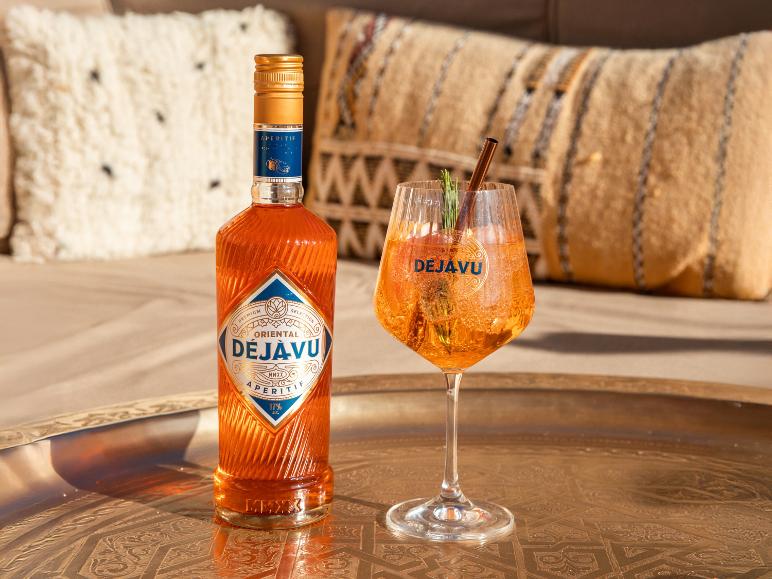 Flasche Orangen-Aperitif und ein Cocktailglas auf einem Tablett, mit Kissen im Hintergrund.