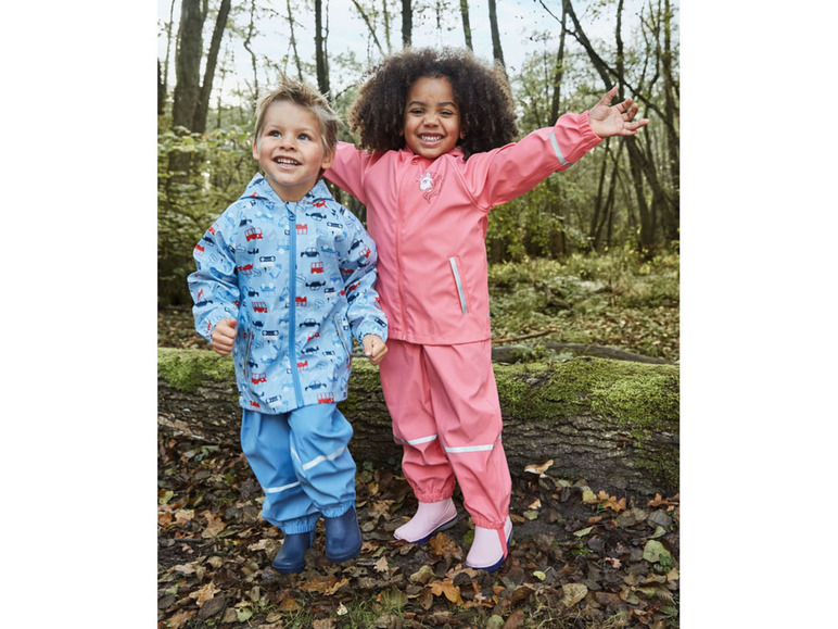 Zwei Kinder in Regenkleidung, eines mit Auto-Print und eines mit rosafarbenem Regenanzug.