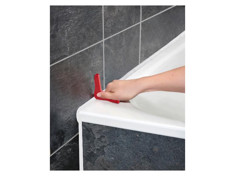 Eine Hand verwendet ein rotes Werkzeug, um Dichtmittel um eine weiße Badewanne aufzutragen.