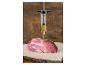 Fleischspritze mit Marinade, mit einem Stück rohem Fleisch auf einem Holzbrett.