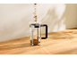 Kaffee wird in eine Glas-French-Press auf einem Holztisch gefüllt.