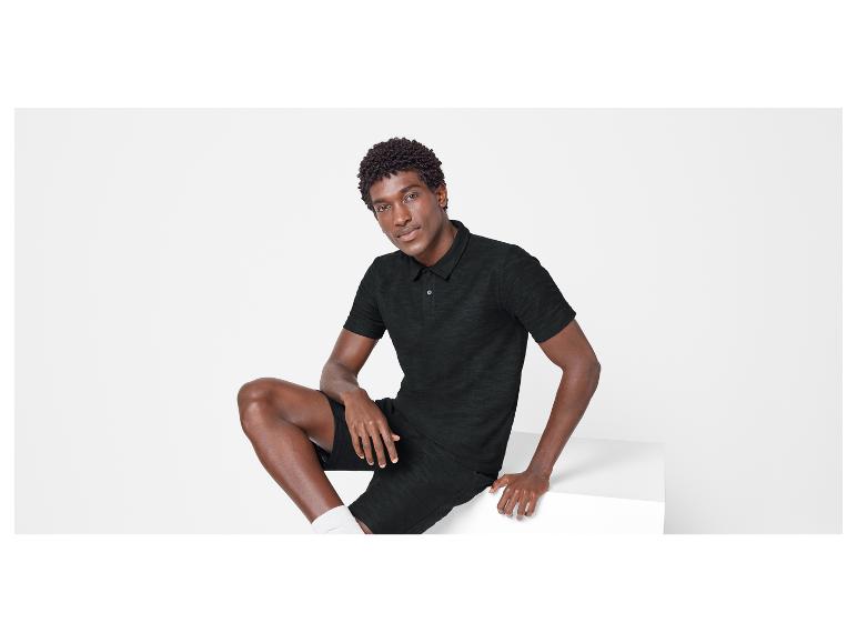 Ein Mann trägt ein schwarzes Poloshirt und Shorts.