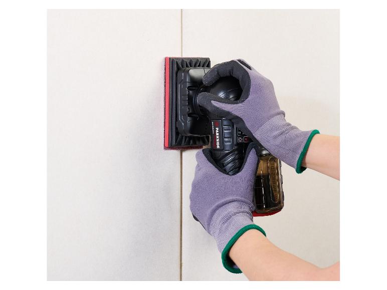 Eine Person schleift eine Wand mit einem Elektroschleifer und trägt Schutzhandschuhe.