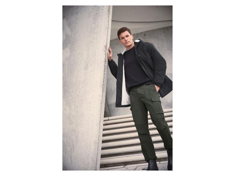 Mann in schwarzer Jacke mit weißem Futter, schwarzem T-Shirt und grüner Cargohose.