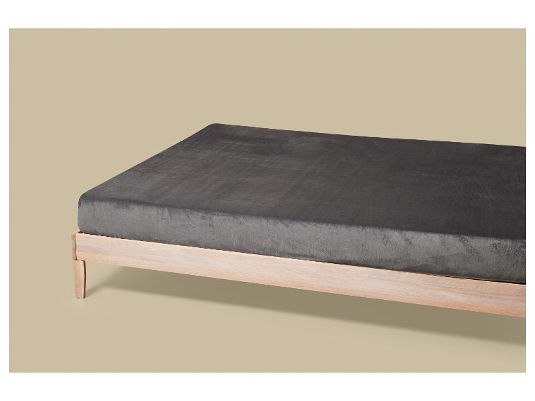 Ein Holzlattenrost mit einem dunkelgrauen Spannbetttuch auf hellbeigem Hintergrund.