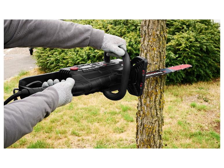 Person in Handschuhen benutzt eine schwarze Elektrokettensäge, um einen Baumstamm im Garten zu schneiden.