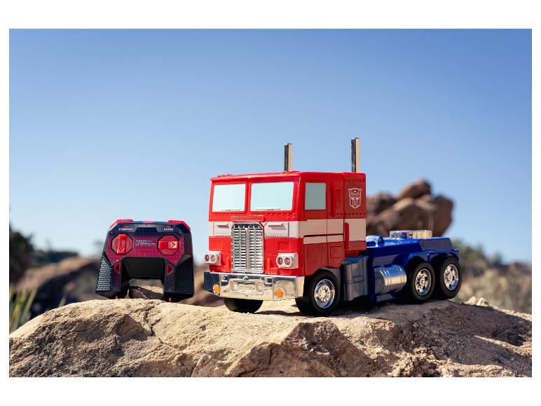 Ein Optimus Prime Spielzeug-LKW und eine Fernbedienung auf felsigem Gelände unter klarem Himmel.