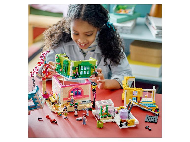 Ein lächelndes Mädchen baut ein LEGO Friends Puppenhaus zusammen, mit anderen Sets drumherum.