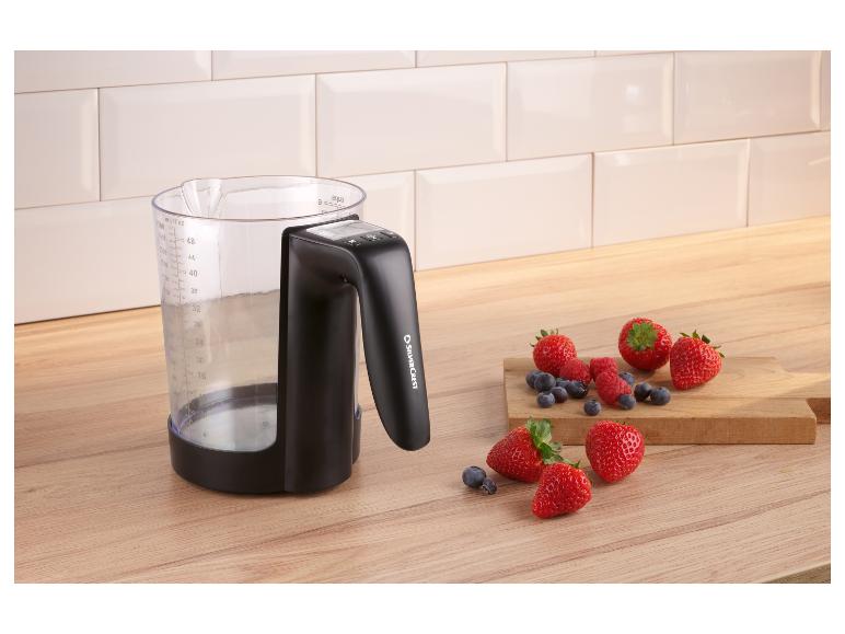 Messbecher mit Griff und Beeren auf einer Holztheke.