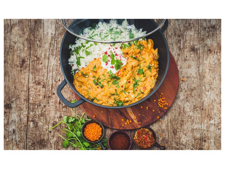 Curry mit Reis und Gewürzen in einem schwarzen Topf auf einem Holztisch.
