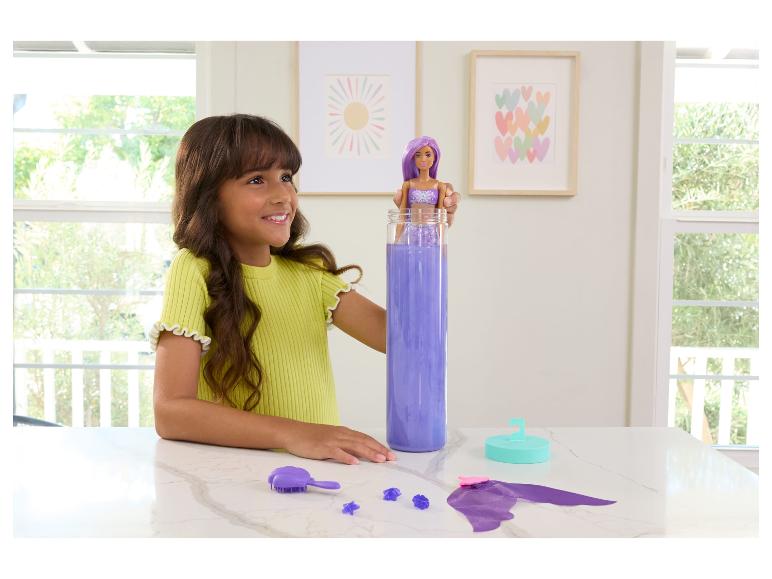 Ein Mädchen spielt mit einer Puppe, die in einem hohen Behälter mit lila Flüssigkeit die Farbe wechselt.