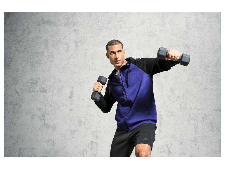 Mann in einem lila Hoodie und schwarzen Shorts mit Kurzhanteln