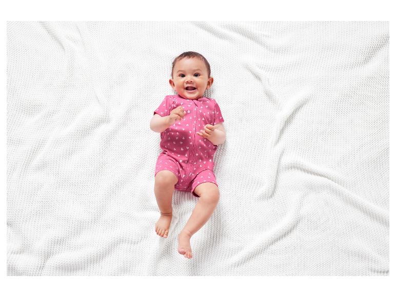 Ein lachendes Baby in einem rosa Strampler mit Herzen.