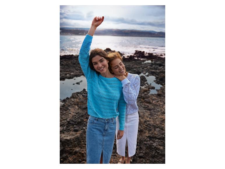 Zwei Frauen in Strickpullovern und Jeansröcken an einem felsigen Strand.