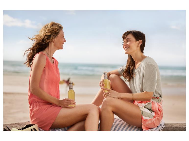 Zwei Frauen trinken Erfrischungsgetränke am Strand.