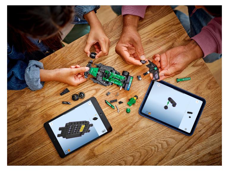 Zwei Personen bauen ein LEGO Rennauto zusammen, den Anweisungen auf Tablets folgend.