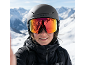 Frau mit Skibrille und Helm vor verschneiten Bergen.