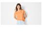 Frau in einem orangefarbenen bestickten T-Shirt und hellen Jeans-Shorts.