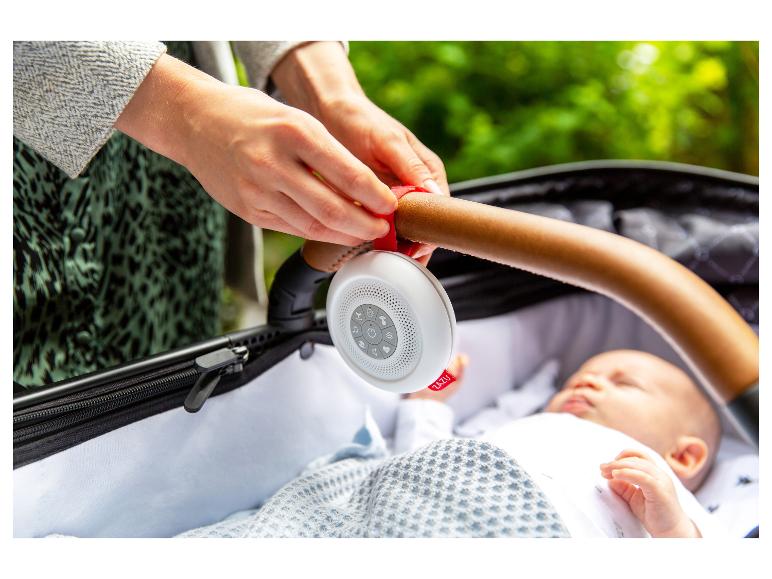 Elternteil befestigt ein weißes ZAZU-Soundgerät am Kinderwagengriff über einem schlafenden Baby.