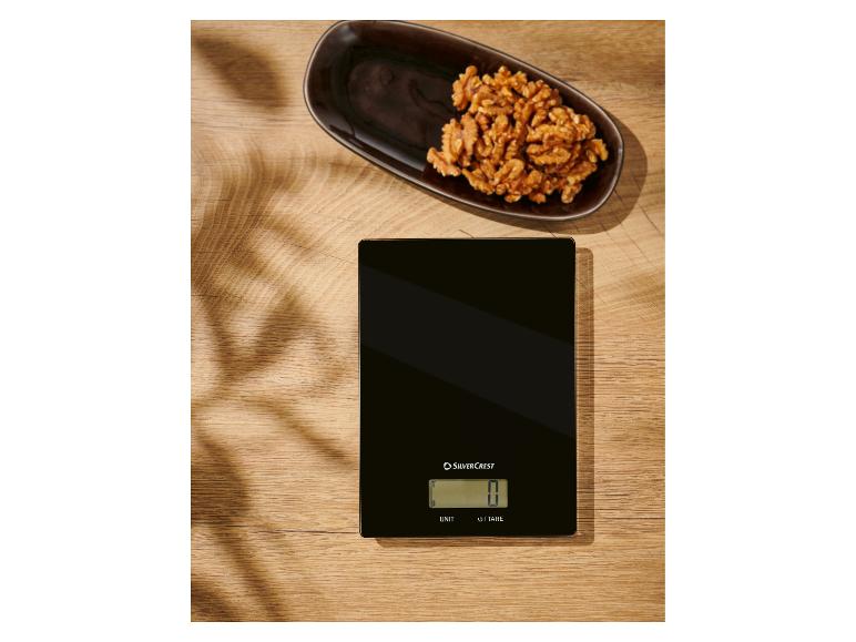 Eine schwarze SilverCrest Küchenwaage auf einem Holztisch mit Walnüssen.