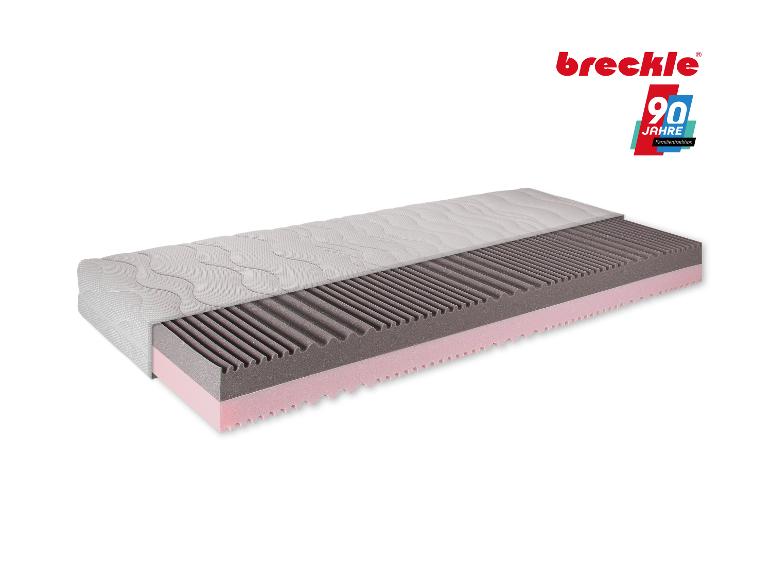 Aufgeschnittene Matratze mit grauen und rosa Schaumstoffschichten und einer weißen, welligen Oberfläche.