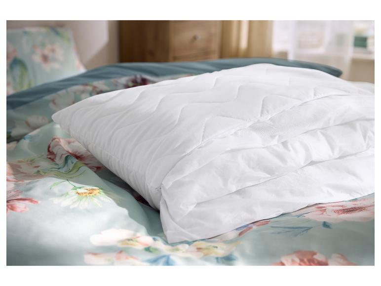 Gesteppter weißer Matratzenschoner auf floraler Bettwäsche in einem Schlafzimmer.