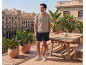Mann in hellgrünem Poloshirt und dunklen Shorts auf einer Terrasse mit Stadtblick.