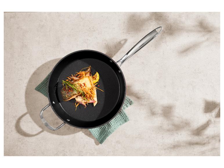 Bratpfanne mit gegrilltem Lachs, Gemüse und Zitrone, auf einem grünen Küchentuch.