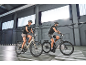 Zwei Personen fahren E-Bikes in Innenräumen, gekleidet in Sportkleidung.