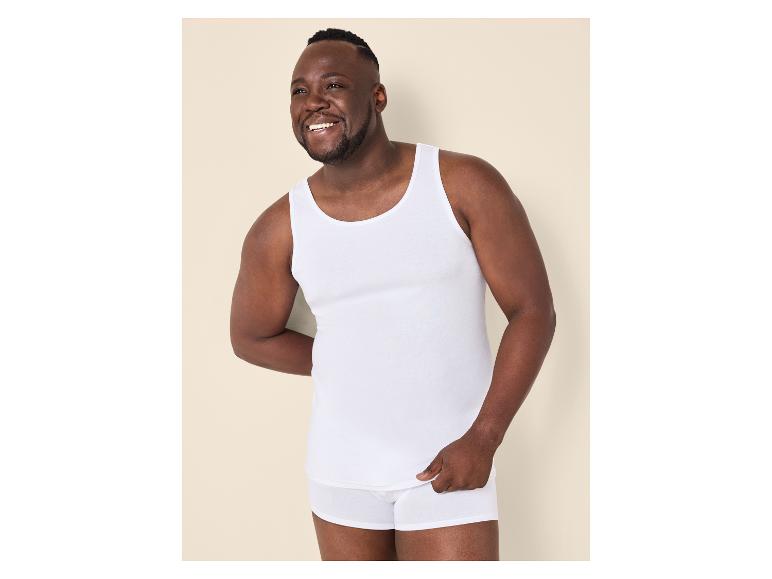 Mann in weißem Unterhemd und Boxershorts, lächelnd.
