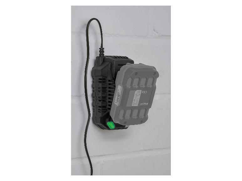 Schwarzes Ladegerät mit angeschlossenem grauem Akku, an einer weißen Ziegelwand montiert.