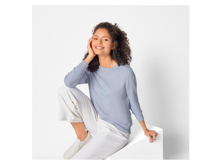 Eine Frau trägt einen blauen Pullover und eine weiße Hose.
