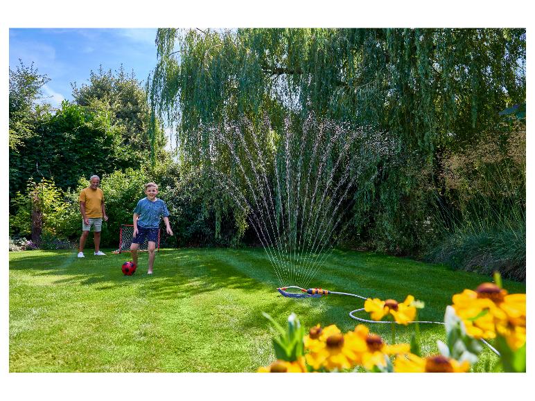 Junge und Mann spielen Fußball im Garten mit einem Rasensprenger.