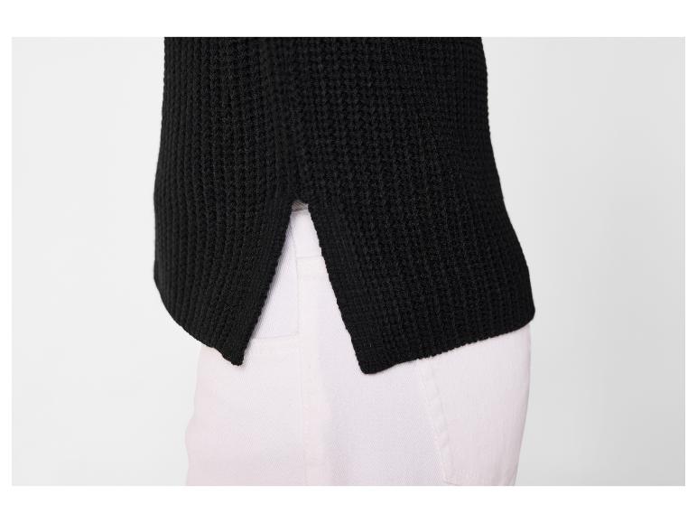Schwarzer Strickpullover mit Seitenschlitzen, über weißer Hose getragen.