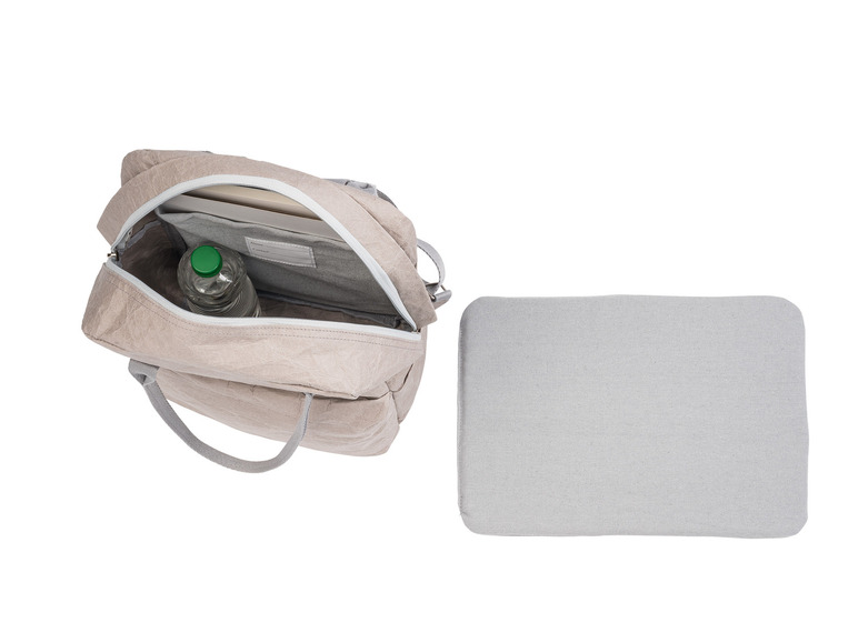 Ein grauer Papierrucksack mit einer Wasserflasche und einem Buch darin, neben einem grauen Untersetzer.