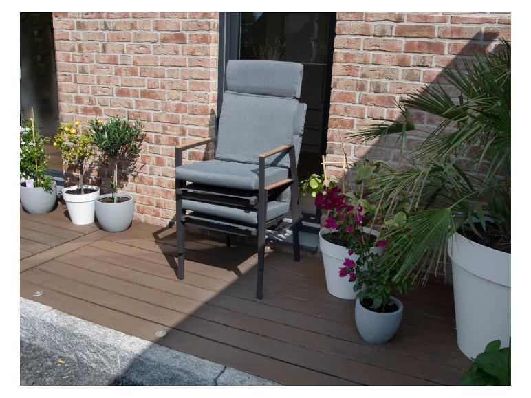 Stapelbare graue Gartenstühle mit Kissen auf einer Holzterrasse mit Pflanzen